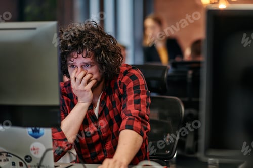 Preview: Disappointed Programmer with Messy Hair Looking at Computer Monitor in Office.