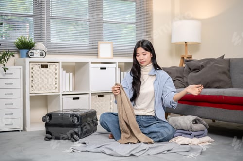 Preview: Asian woman looking at cloth packing or organizing luggage for trip on bedroom or living room floor.