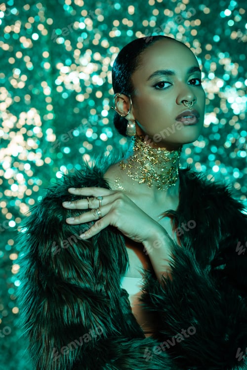 Preview: Stylish african american woman in faux fur jacket and foil on neck looking at camera on sparkling