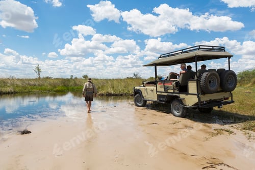 Preview: A safari vehicle with passengers, and a guide walking across sand