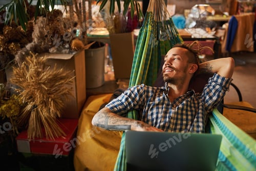 Preview: Handsome young man lying in hammock and using notebook