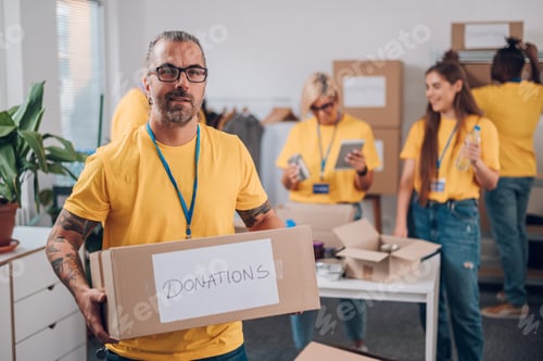 Preview: Portrait of a volunteer holding cardboard box with his colleagues in the background