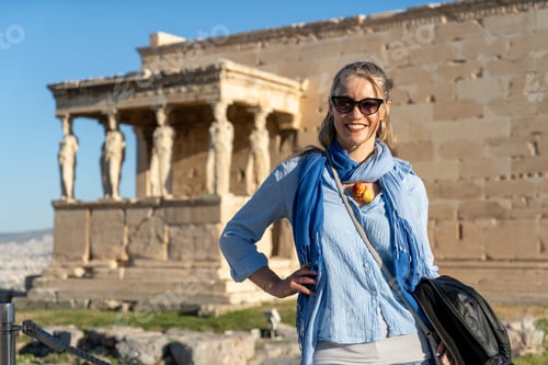 Preview: Vertical shot of a Caucasian blonde woman posing in front of Acropolis, Athens