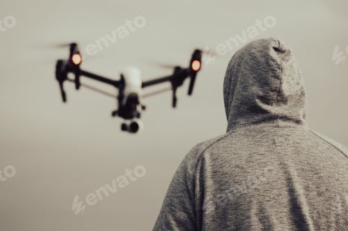 Preview: Back shot of a hoodie male looking at a flying blur drone in the gray sky