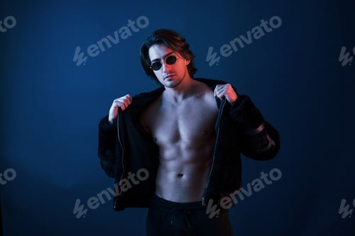 Preview: Beautiful man in glasses and black clothes is in the studio with blue neon lighting