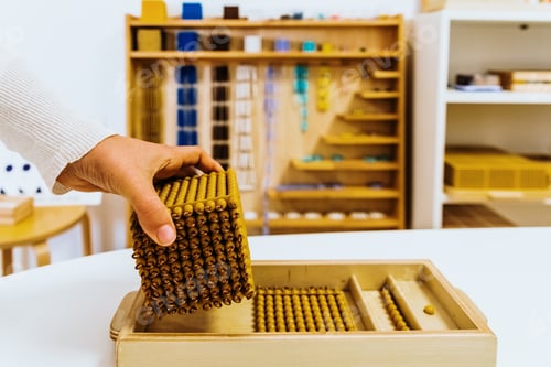 Preview: Hand of a student handling montessori material inside a classroom.