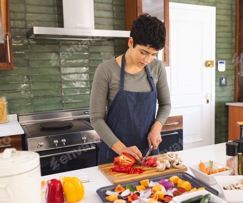 Preview: woman chopping red bell peppers on wooden cutting board in home kitchen, with spice jars