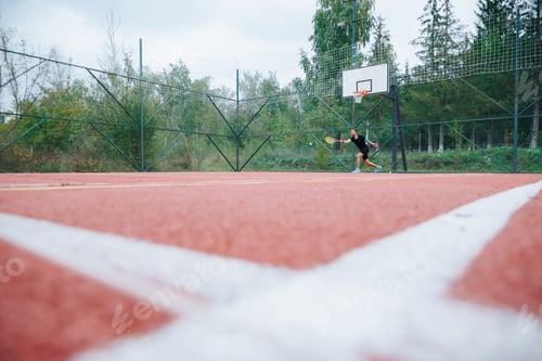 Preview: A tennis player dressed in black focuses on hitting the ball outdoors
