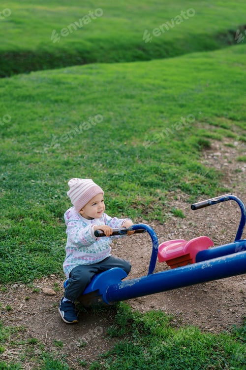 Preview: Little smiling girl sits on a swing-balancer holding the handle