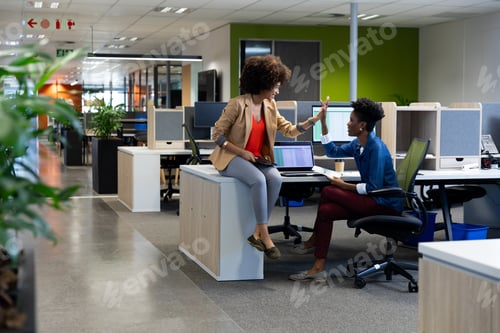 Preview: Happy biracial businesswomen giving high-five in meeting while sitting in cubicle at workplace