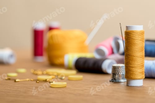 Preview: selective focus of thread coil with clothing buttons on wooden table isolated on beige