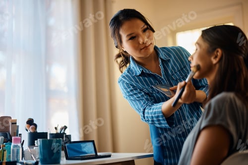 Preview: Young Asian beautician applying blush on woman's cheek.