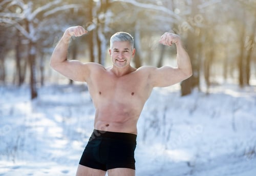 Preview: Handsome senior man with bare torso showing his strong biceps in winter frost at snowy forest
