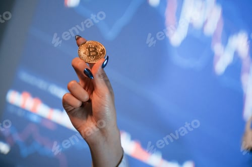 Preview: Close up view of woman's hand that holding physical bitcoin against background with graphs