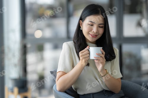 Preview: Attractive young Asian woman or businesswoman sitting drinking and holding cup of coffee relaxing, t