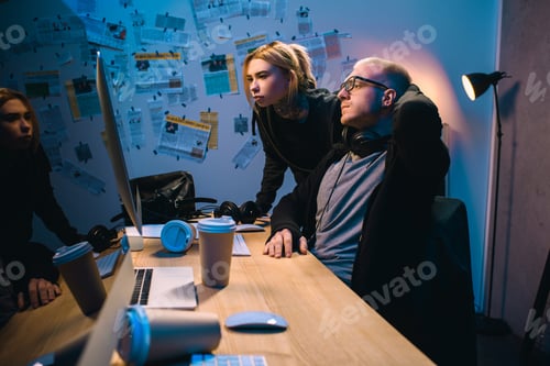 Preview: couple of hackers looking at computer screen together in dark room