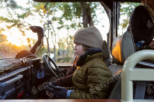 Preview: A boy in a hat and coat in a jeep at sunrise on a safari drive.