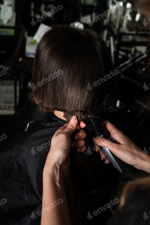 Preview: Clippers used for female haircut. Hairdresser trims brunette client for a new short hairstyle