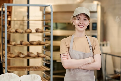 Preview: Smiling young woman standing in bakery kitchen with arms crossed