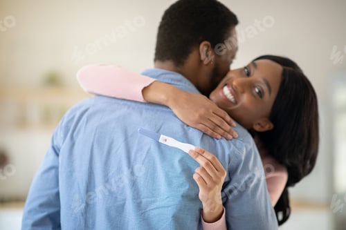 Preview: Millennial balck couple excited about positive results of pregnancy test, hugging each other at home