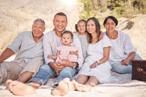 Preview: Portrait of a smiling mixed race family with little girls sitting together at the beach. Adorable