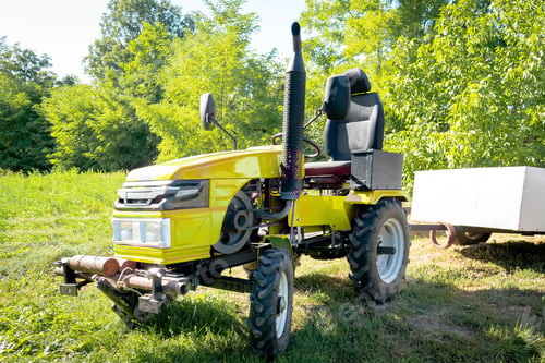 Preview: Small mini yellow modern new tractor with trailer standing at farm, field, nature countryside