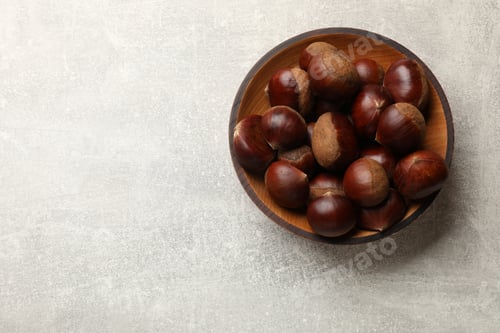 Preview: Roasted edible sweet chestnuts in bowl on light grey table, top view. Space for text