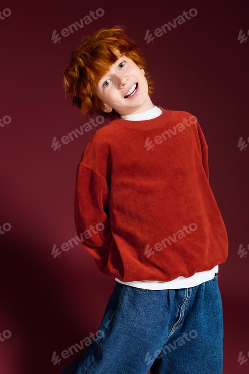 Preview: Playful redhead boy dressed in cozy fashion poses in vibrant studio setting