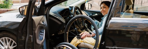 Preview: Brunette woman holding wheelchair while getting into car on city street