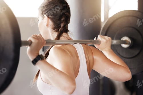 Preview: One unknown caucasian athlete lifting barbell during back squat workout in gym. Fit, active woman t