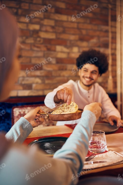 Preview: Close-up of Middle Easter woman serving pita bread to her husband during a meal at dining table.