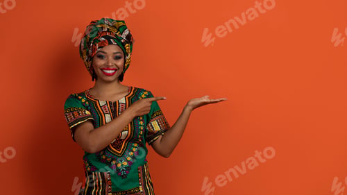 Preview: Happy attractive african woman in national costume showing something nice