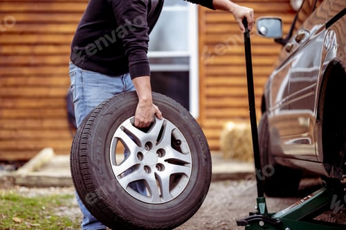 Preview: Selective focus shot of a man changing a tire of a car