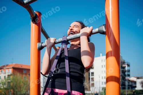 Preview: Calisthenics at outdoor gym, young woman doing pull up on exercise equipment