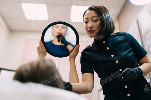 Preview: Girl looking at lips in mirror near beautician