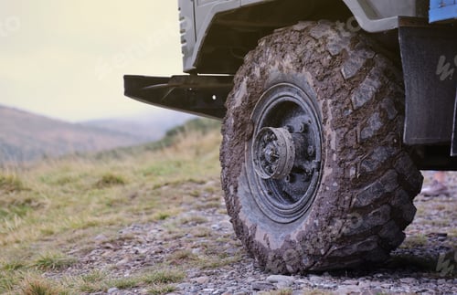 Preview: Wheel closeup in a countryside landscape with a mud road. Off-road 4x4 suv automobile with