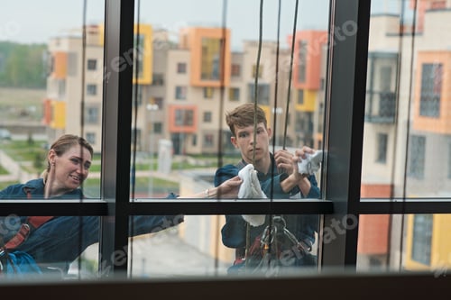 Preview: Brave industrial climbers on safety ropes washing the facade of a build. Small business concept
