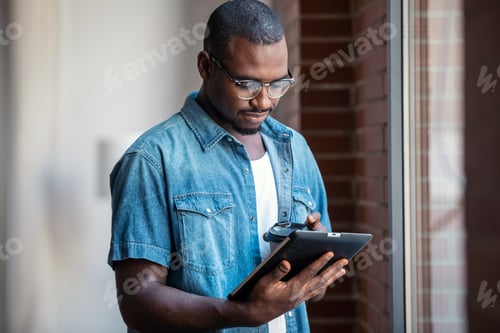 Preview: Confident businessman working with digital tablet while standing near windows in a coworking space.