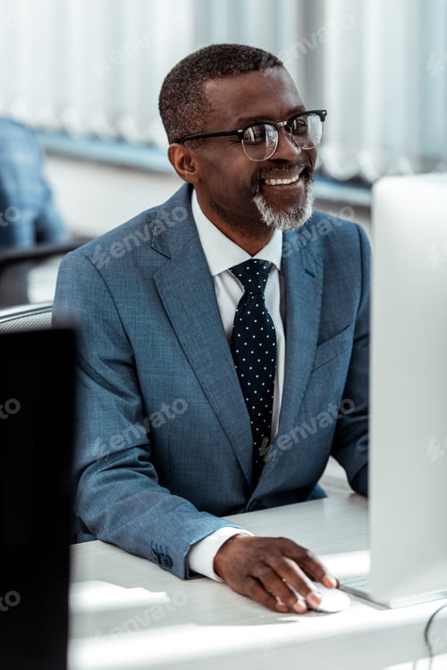 Preview: selective focus of happy african american businessman looking at computer monitor in office