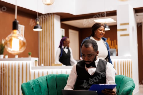 Preview: Man bellboy using laptop in hotel lobby