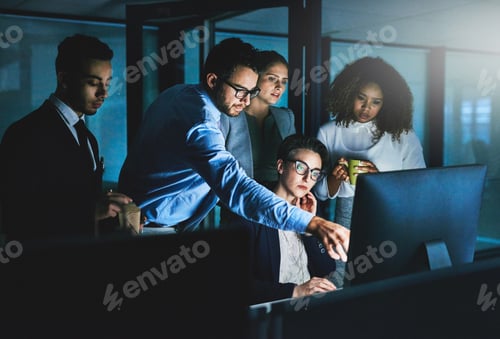 Preview: Shot of colleagues standing together as they work on something on a computer at night