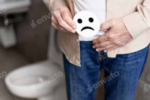 Preview: Senior man holding sad face emoticon near groin in bathroom: prostate problems concept