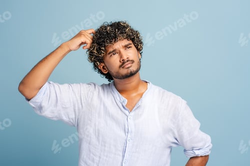 Preview: Young man scratching head thinking and looking up isolated on blue background