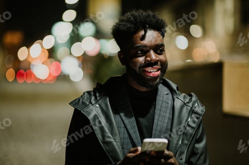 Preview: Portrait of a young urban African American man using his phone on a city street at night.