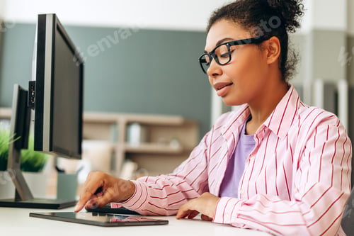 Preview: African American office worker using digital tablet and computer at desk