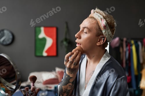 Preview: Tattooed Young Man Doing Makeup at Home and Looking in Mirror
