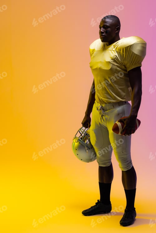 Preview: African american male american football player holding ball with neon yellow and purple lighting