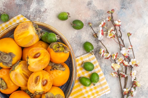 Preview: top view delicious persimmons in a bowl yellow kitchen towel feykhoas apricot blossom branch on nude