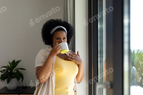 Preview: Thoughtful plus size african american woman looking out of window drinking coffee