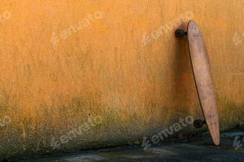 Preview: Worn skate longboard leaning against the dirty orange wall